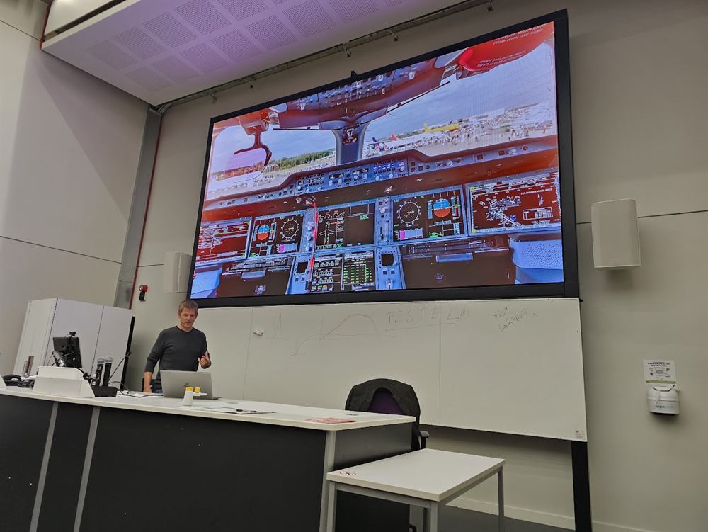 A speaker presenting with an aircraft cockpit on screen